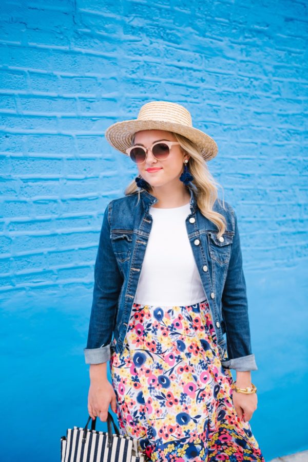 Bows & Sequins wearing a dark wash denim jacket, a floral Hutch dress from Anthropologie, and a L Space straw hat with aviators.