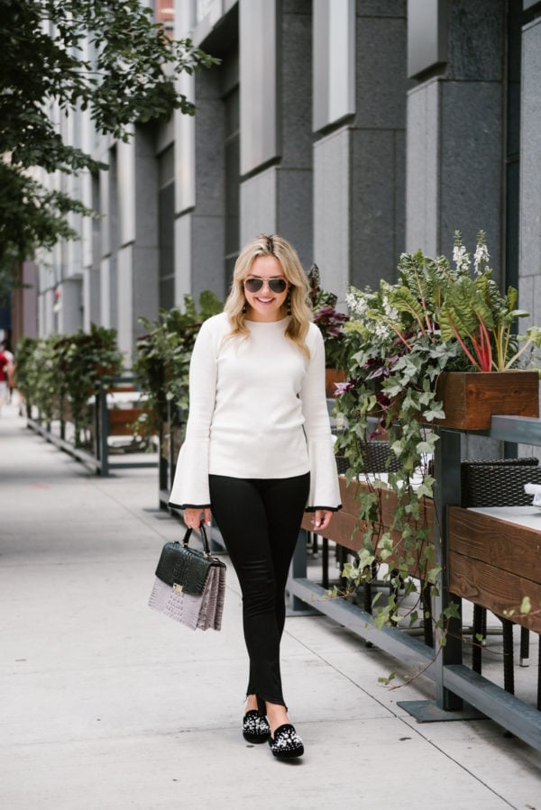 Bows & Sequins, a Chicago-based lifestyle blogger, wearing a Halogen bell sleeve sweater from Nordstrom, black Paige raw hem jeans, embellished pearl slides, and Gucci aviators with a Brahmin handbag.