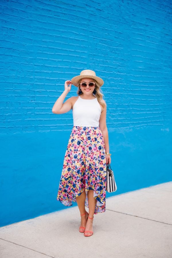 Bows & Sequins wearing a high-low floral dress with a straw hat and coral ankle strap heels in Chicago.