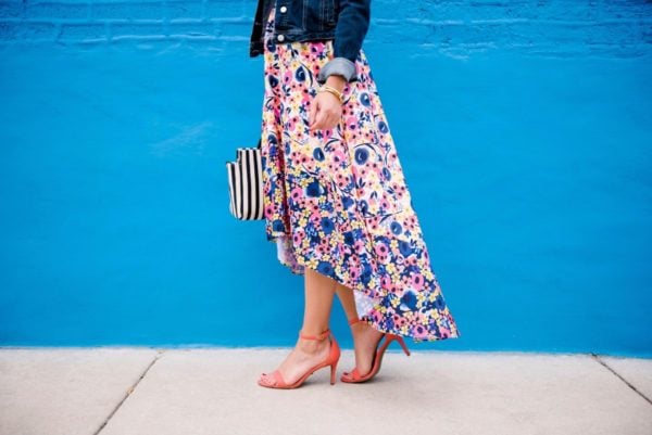 Chicago lifestyle blogger Bows & Sequins wearing a floral high-low dress from Anthropologie with coral ankle strap heels from Old Navy with a Clare V striped tote and a denim jacket.