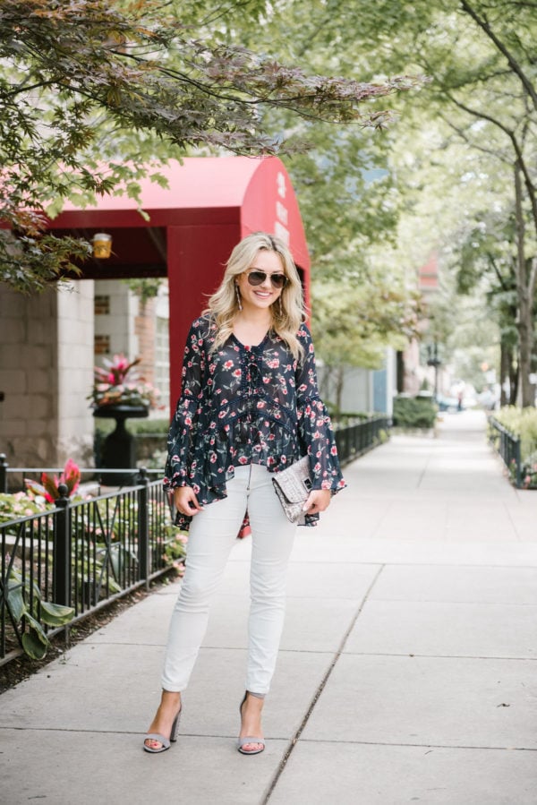 Bows & Sequins wearing a floral Moon River blouse with Vineyard Vines white corduroy jeans, Dolce Vita studded heels, and metallic silver clutch.