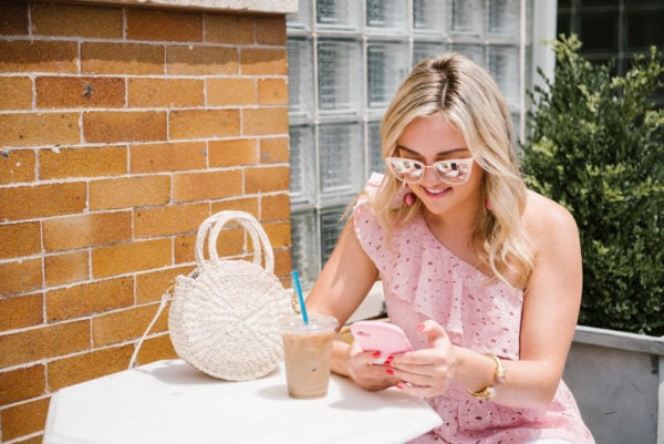 Bows & Sequins wearing a one shoulder eyelet top with blush pink sunglasses and a natural straw tote.