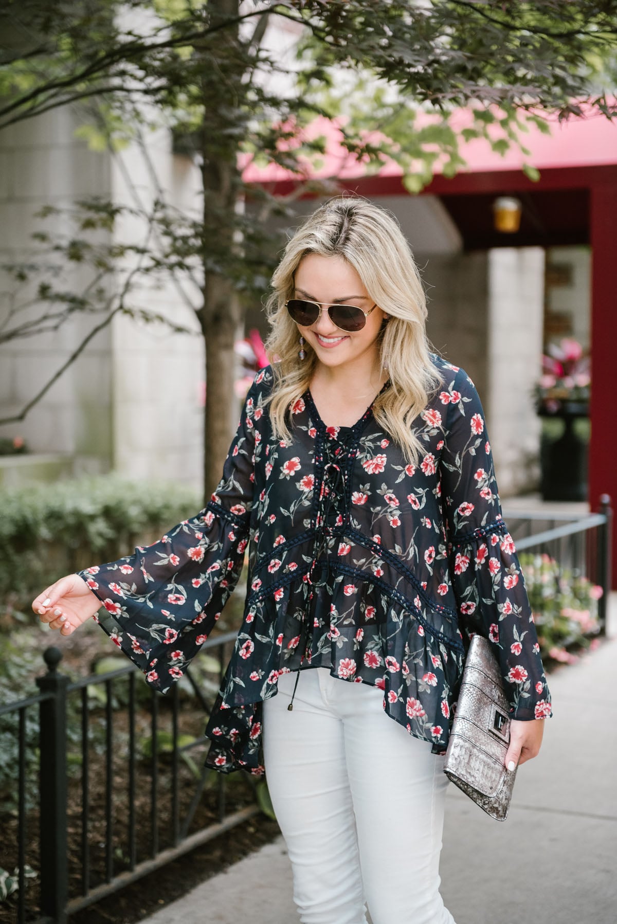 Bows & Sequins wearing a Moon River flare sleeve floral blouse with a metallic silver clutch and Gucci aviators.