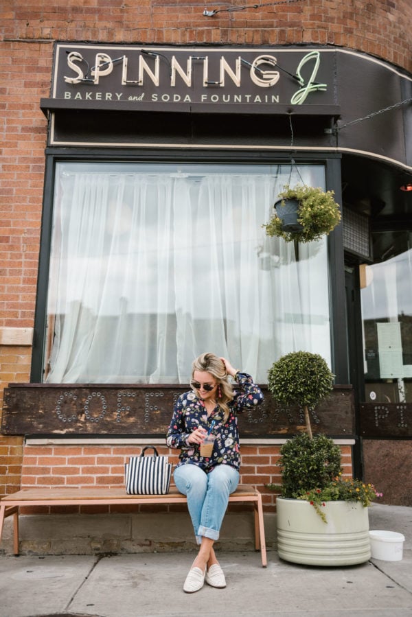 Bows & Sequins wearing a floral blouse, cuffed straight leg denim, and white leather loafers at a coffee shop in Chicago.