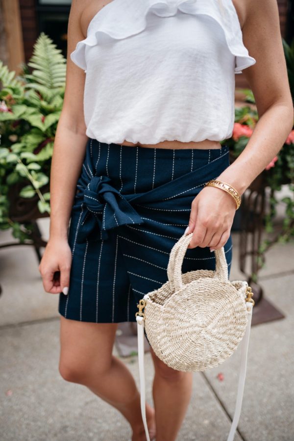 Bows & Sequins holding a Clare V straw tote and wearing a J.O.A. tie-front pinstripe skirt and a Chanel bracelet via Switch.