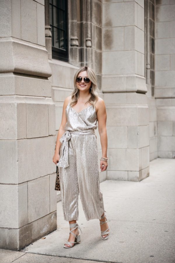 Bows & Sequins wearing a metallic gold jumpsuit with Gucci aviators, grey suede block heel sandals, a leopard clutch, and pavé bracelets.