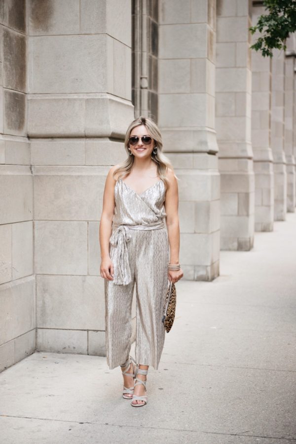 Bows & Sequins styling a metallic gold Plissé jumpsuit with Gucci aviator sunglasses, pavé bracelets, gray suede heels, Loren Hope earrings, and a Clare V clutch.
