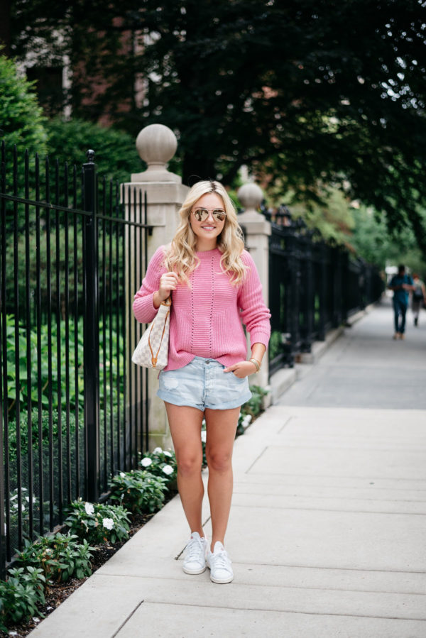 Bows & Sequins wearing a pink sweater with jean shorts and sneakers.