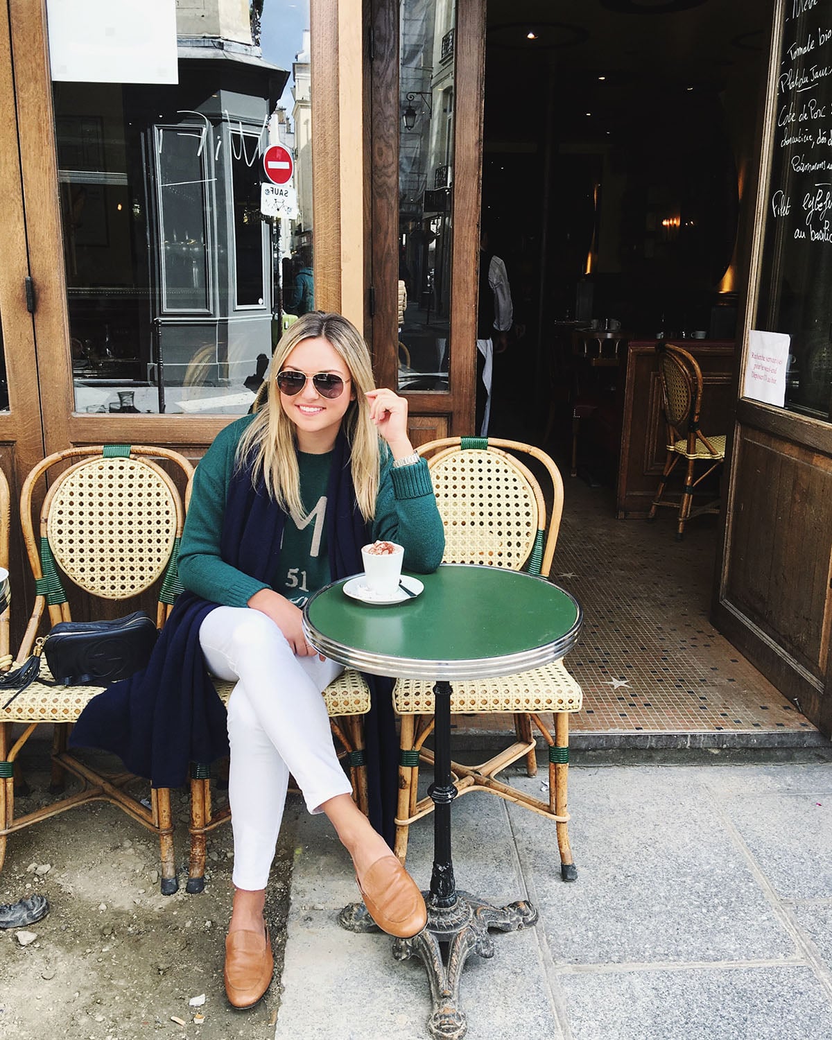 Jessica Sturdy wearing white jeans during the fall in Paris. Styled with leather loafers, a hunter green sweater, a navy cashmere scarf, and a Gucci handbag and sunglasses.