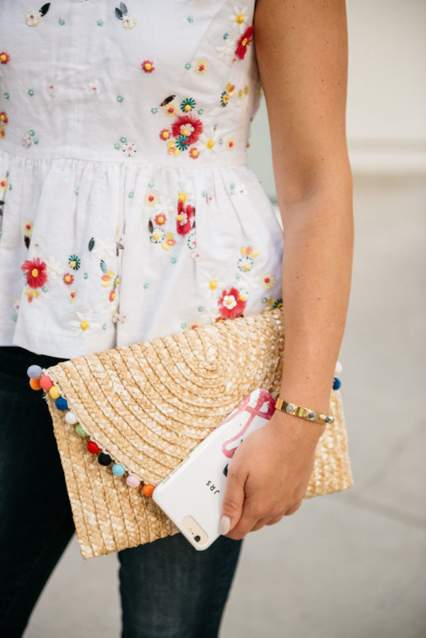 Bows & Sequins wearing a J.Crew embroidered peplum top and a BaubleBar cuff, holding a White Elephant Designs pom pom straw clutch and a Minnie & Emma flamingo phone case.