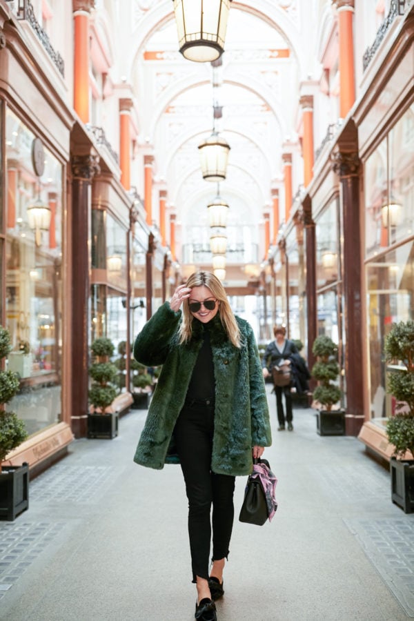 Bows & Sequins wearing a black turtleneck bodysuit, black jeans, bow mules, and a green fur coat in London.