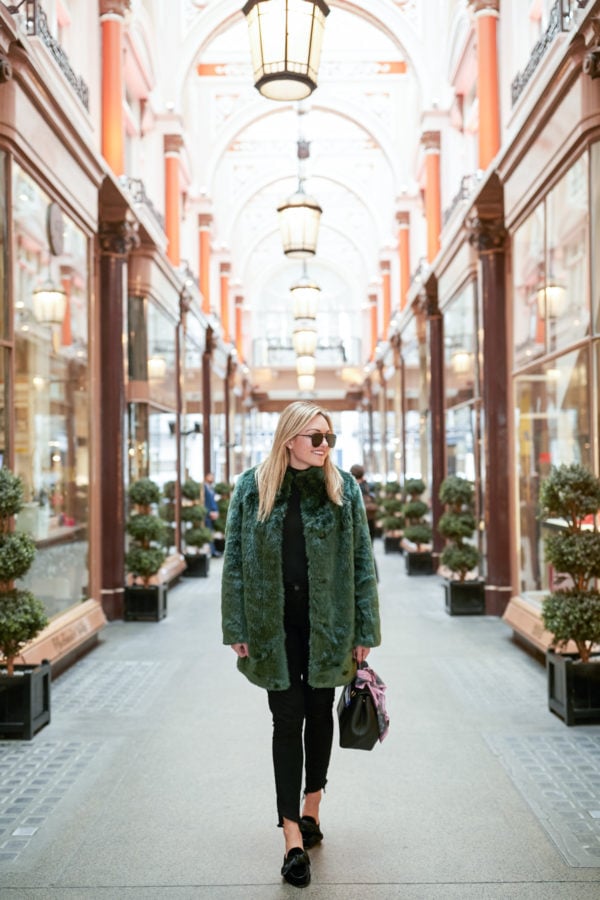 Bows & Sequins wearing a turtleneck bodysuit, black jeans, bow mules, black aviators, a Polene bag, and a faux fur green coat in London.