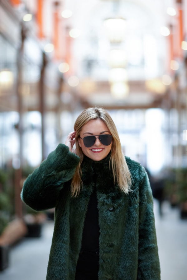 Bows & Sequins wearing matte black aviators and a green faux fur jacket in London.