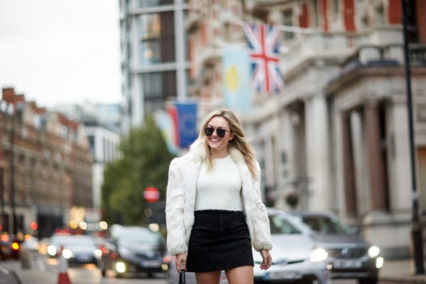 Travel and fashion blogger Bows & Sequins wearing a vintage white fur coat, a white crop top, and an H&M black suede skirt with matte black aviators.