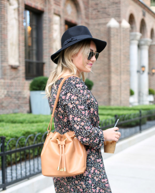 Fashion and lifestyle blogger Bows & Sequins wearing a black Old Navy hat, Ray-Ban aviators, and a floral dress with a Brahmin leather bag.