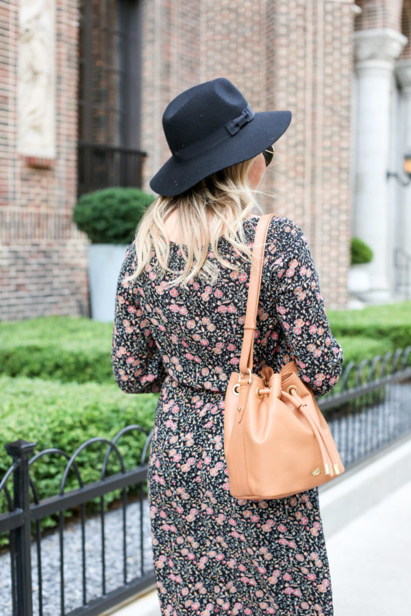 Bows & Sequins wearing a black Old Navy hat, a floral dress, and a Brahmin leather bucket bag.