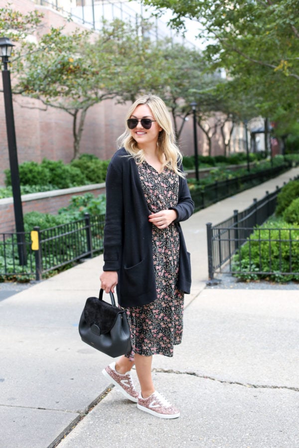 Bows & Sequins wearing a long black cardigan, a floral midi dress, glitter sneakers, and a Polene top-handle leather bag.