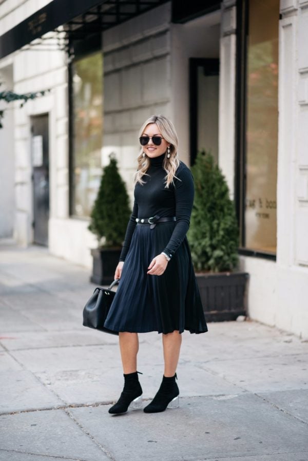 Bows & Sequins wearing Baublebar earrings, a J.Crew turtleneck bodysuit, a Leith pleated skirt, and Steve Madden lucite ankle boots.