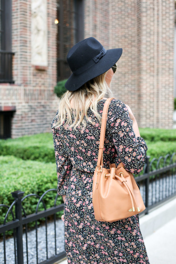 Bows & Sequins wearing a black hat from Old Navy, a floral dress, and a tan leather Brahmin bucket bag.