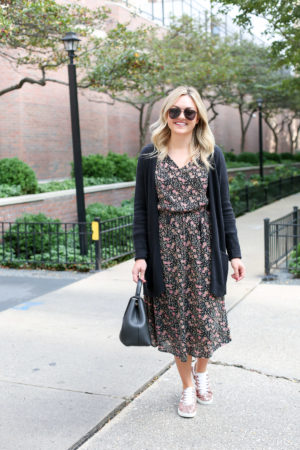 Bows & Sequins wearing aviators, a black cardigan, floral midi dress, and pink glitter sneakers with a Polene top-handle leather bag.