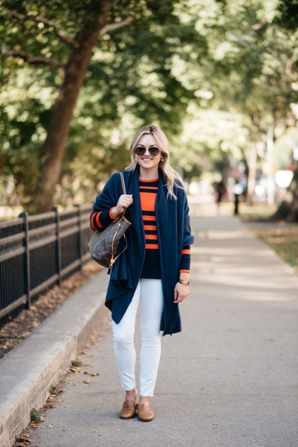 Chicago fashion and lifestyle blogger Bows & Sequins wearing a navy blue cashmere wrap, an orange and blue striped sweater, and white denim with Gucci aviators and Dune London leather loafers.