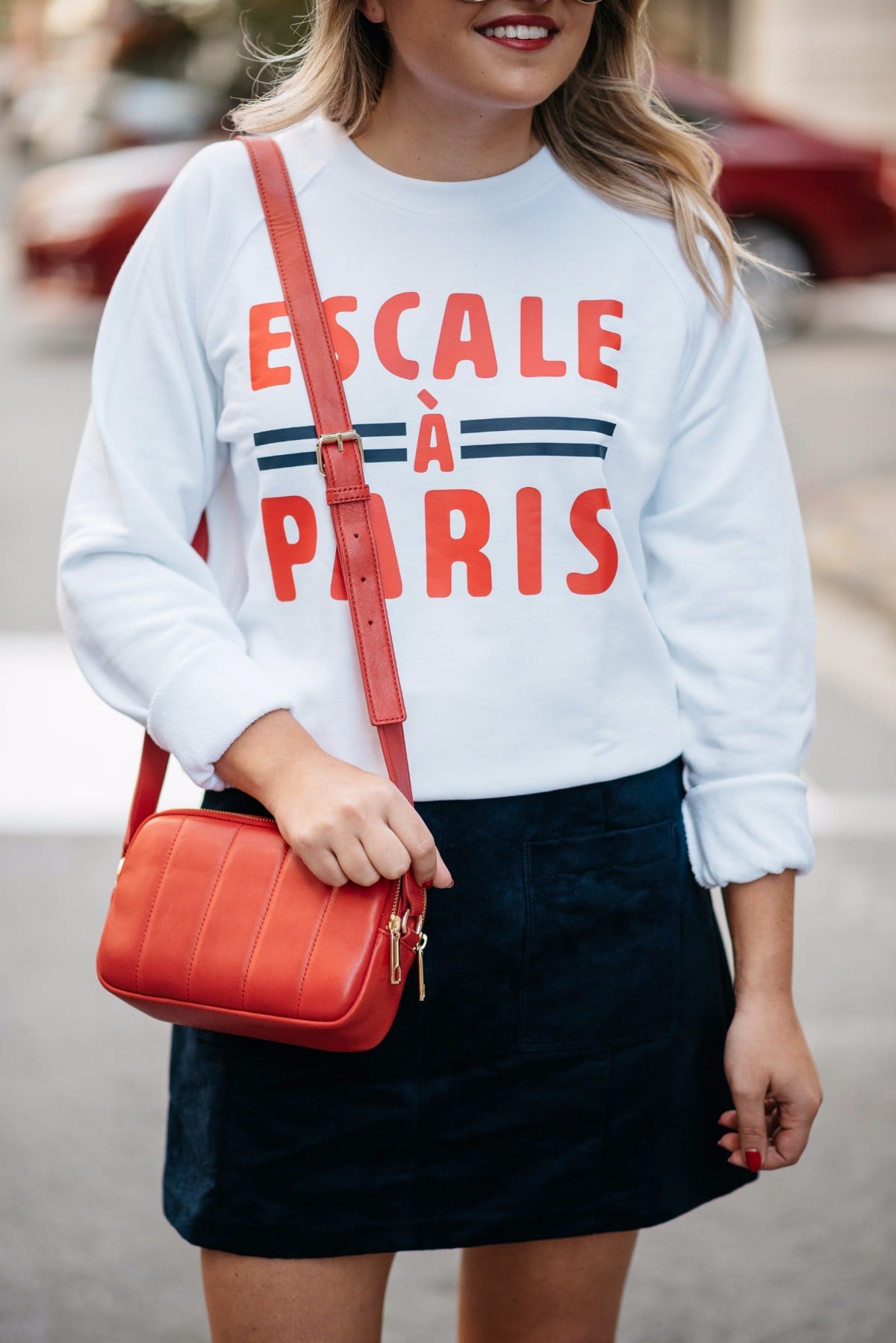 Chicago-based lifestyle blogger Bows & Sequins wearing a French Disorder sweatshirt with a Talbots red leather shoulder bag and a blue suede skirt.
