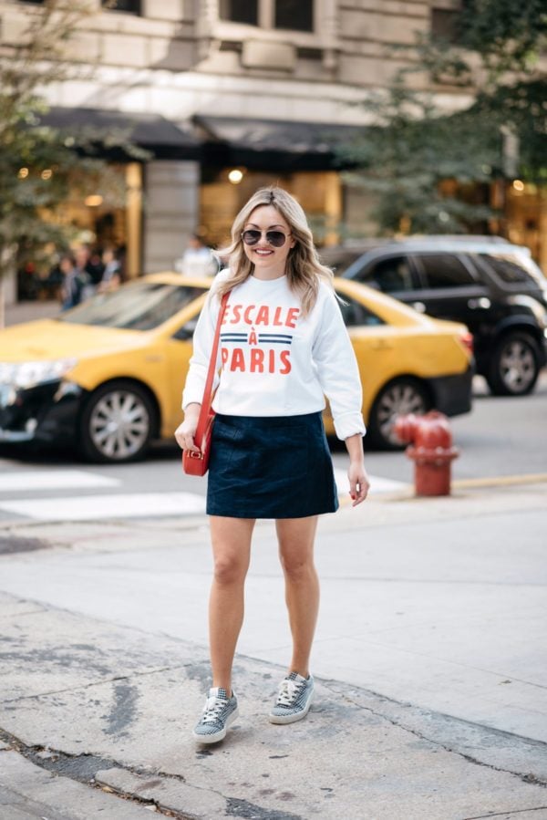Fashion-focused lifestyle blogger Bows & Sequins wearing Gucci aviators, a French Disorder Paris sweatshirt, and an Old Navy blue suede skirt and Claudie Pierlot gingham sneakers with a Talbots red leather bag.