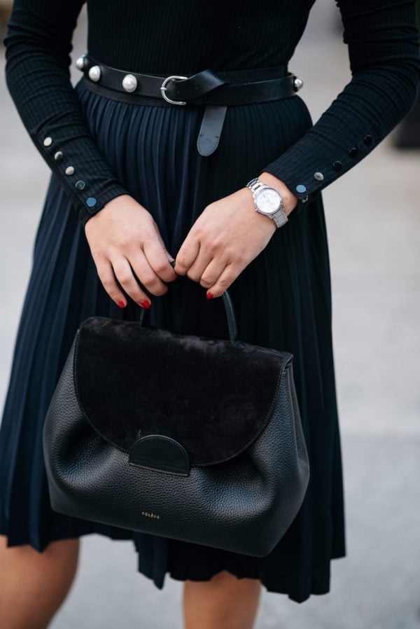Bows & Sequins wearing a silver watch, a Claudie Pierlot pearl studded belt, a black and navy pleated skirt, and a Polene leather top-handle bag.