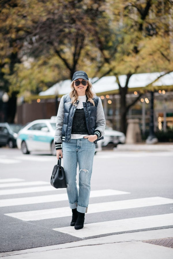 Jessica Sturdy wearing a baseball cap, Le Specs matte black aviators, a Veronica Beard puffer bomber jacket, an Endless Rose layered tee and crochet tank, Levi 501 Jeans, Steve Madden lucite booties, and a Polene Paris top-handle bag.