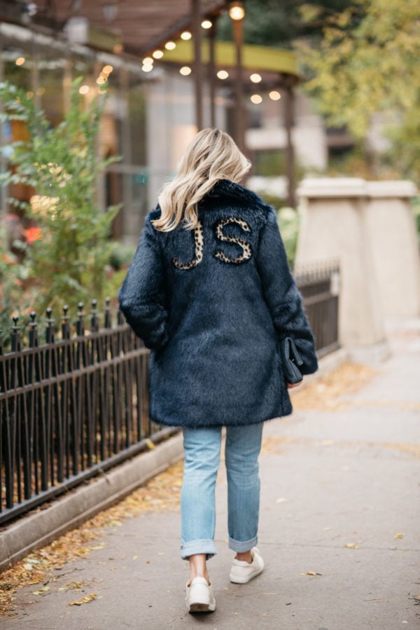 Fashion and lifestyle blogger Jessica Rose Sturdy wearing a leopard-print monogrammed faux fur Miranda Dunn coat with Illesteva sunglasses, Vineyard Vines boyfriend jeans, and Sezane Paris Jack leather sneakers.