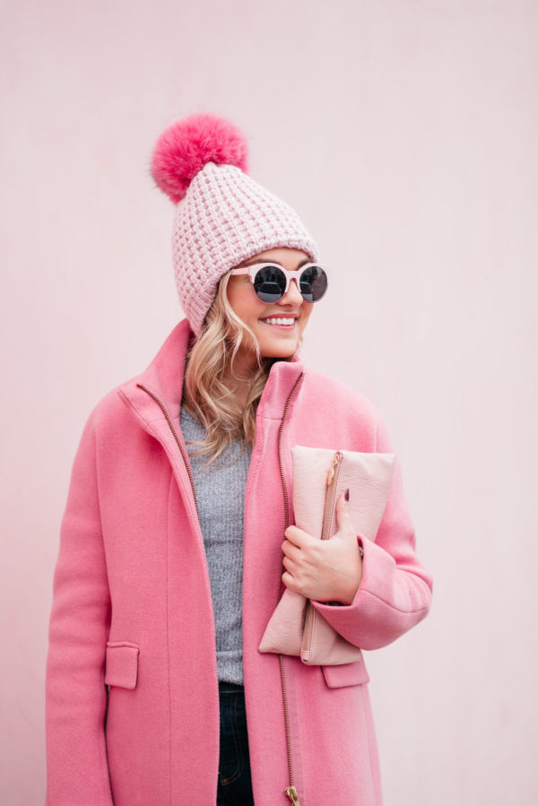 Fashion blogger Jessica Rose Sturdy wearing pink sunglasses, a pink pom pom hat, a blush pink clutch, and a J.Crew cocoon coat.
