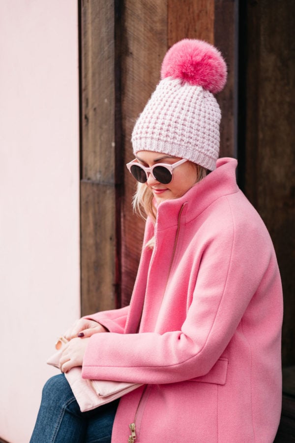 Fashion blogger Jessica Rose Sturdy wearing pink sunglasses, a pink pom pom hat, a blush pink foldover clutch, and a J.Crew cocoon coat.