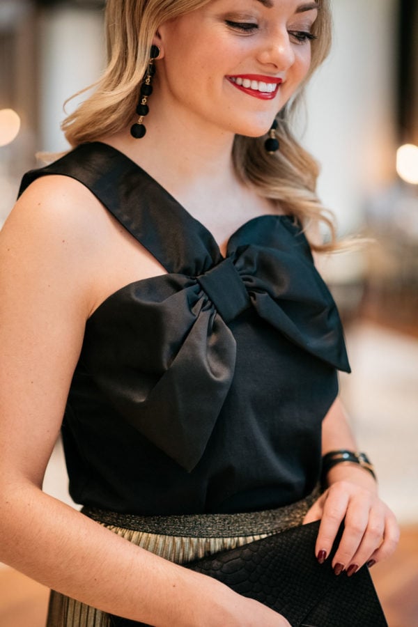 Jessica Sturdy wearing Baublebar black ball earrings, a black and gold cuff, and J.Crew black bow top.