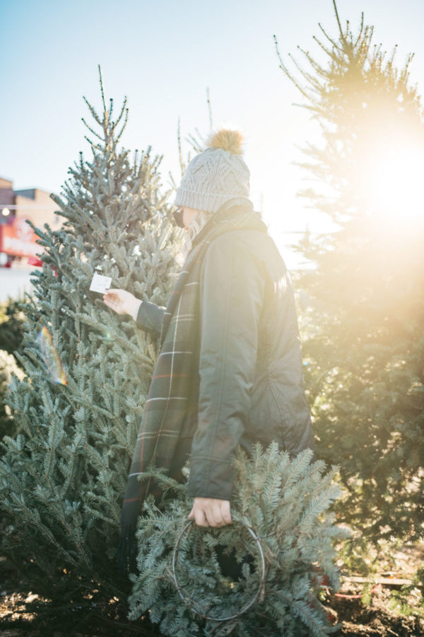 Jessica Sturdy wearing a fur pom hat, a black Beadnell jacket, and a tartan Barbour scarf at a Christmas tree farm in Chicago.