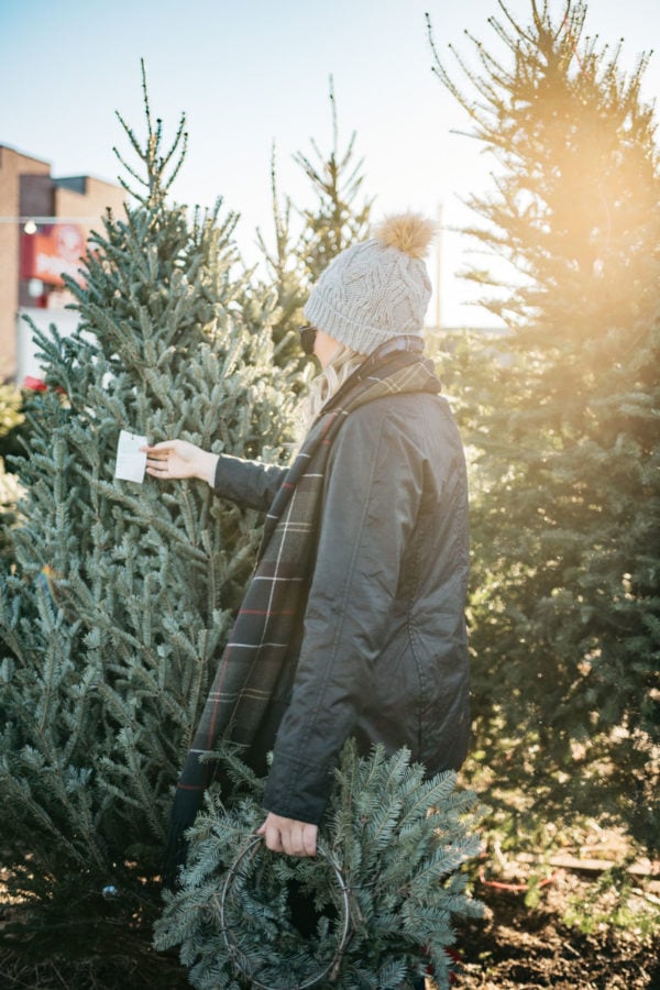 Jessica Sturdy wearing a fur pom hat, a black Beadnell jacket, and a tartan Barbour scarf at a Christmas tree farm in Chicago.