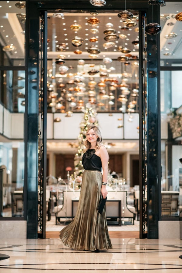 Jessica Rose Sturdy wearing a J.Crew black bow top, Eliza J gold pleated maxi skirt, Marc Fisher black velvet pumps, and a Baublebar black and gold cuff with a black envelope clutch at the Langham in Chicago.
