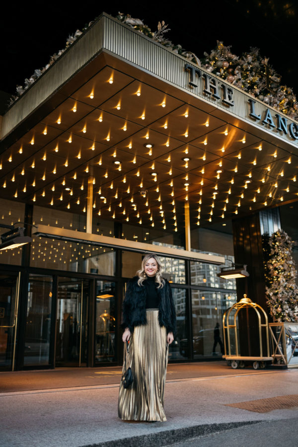 Jessica Sturdy wearing a 1.State black faux fur jacket, black turtleneck, Eliza J gold pleated maxi skirt, Kenneth Jay Lane gold ball earrings, Marc Fisher velvet pumps, and Dolce & Gabbana red lipstick with a Gucci Marmont bag at the Langham in Chicago.