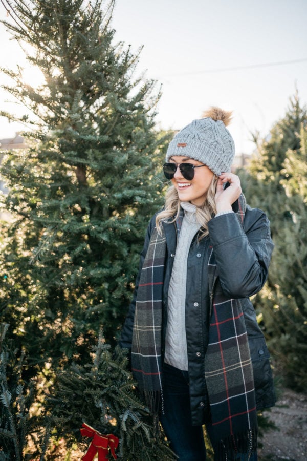 Fashion blogger Jessica Rose Sturdy wearing a Barbour cable knit fur pom hat, Le Specs matte black aviators, and a Barbour tartan scarf with a black Barbour Beadnell.