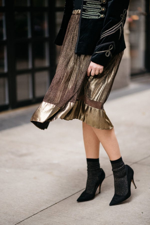 Jessica Sturdy wearing a metallic gold pleated midi skirt and Swildens black and gold shimmer socks with Kate Spade black suede Licorice pumps.