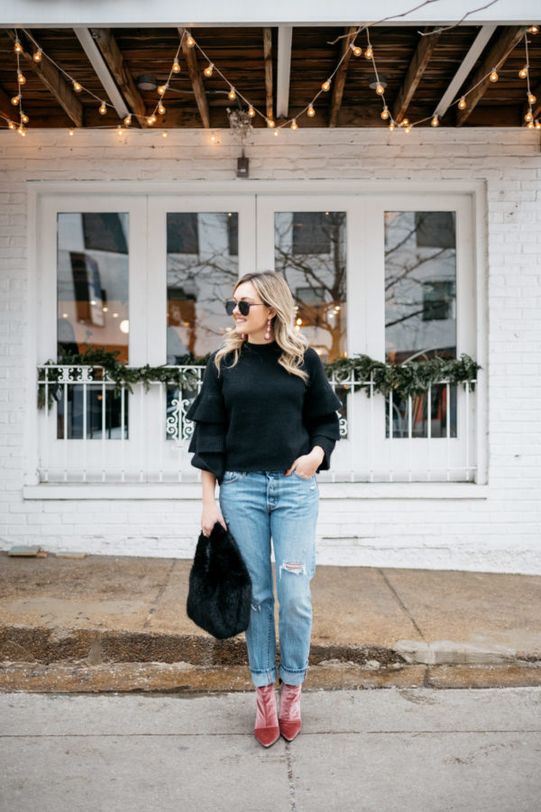 Jessica Sturdy wearing a black ruffle sleeve sweater, Levi's 501 boyfriend jeans, aviators, and pink velvet booties with a black fur bag.