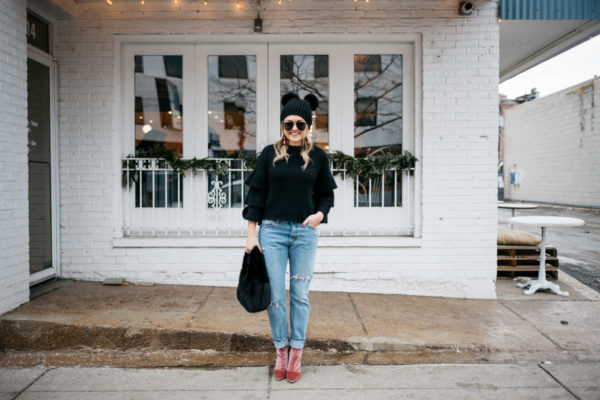 Jessica Rose Sturdy wearing a black ruffle sleeve sweater, Levi's 501 boyfriend jeans, aviators, and pink velvet booties with a black fur bag and pom pom beanie.