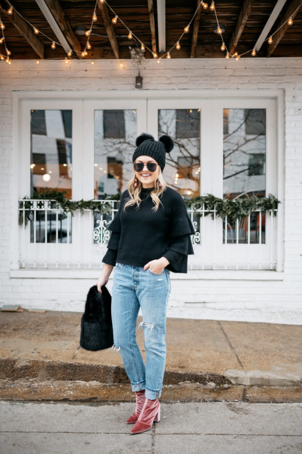 Lifestyle blogger Jessica Rose Sturdy wearing a black ruffle sleeve sweater, pink drop earrings, Levi's 501 boyfriend jeans, aviators, and pink velvet booties with a black fur bag and pom pom beanie at Maison Marcel in Chicago.