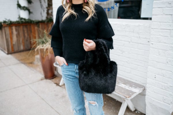 Fashion and lifestyle blogger Jessica Sturdy wearing a black ruffle sleeve sweater with boyfriend jeans and a black fur bag at Maison Marcel in Chicago.
