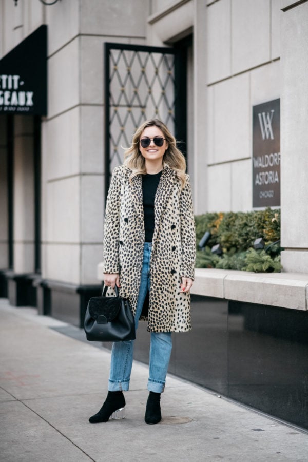 Jessica Sturdy wearing Le Specs matte black Prince aviators, Bows & Sequins leopard coat, Old Navy black ribbed sweater, Levi's 501 boyfriend jeans, and Steve Madden lucite booties with a Polene Paris black top-handle bag.