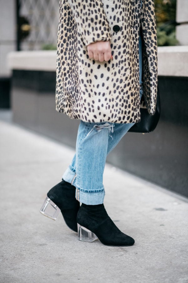 Jessica Sturdy wearing Le Specs matte black Prince aviators, Bows & Sequins leopard coat, Levi's 501 boyfriend jeans, and Steve Madden lucite booties with a Polene Paris black top-handle bag.
