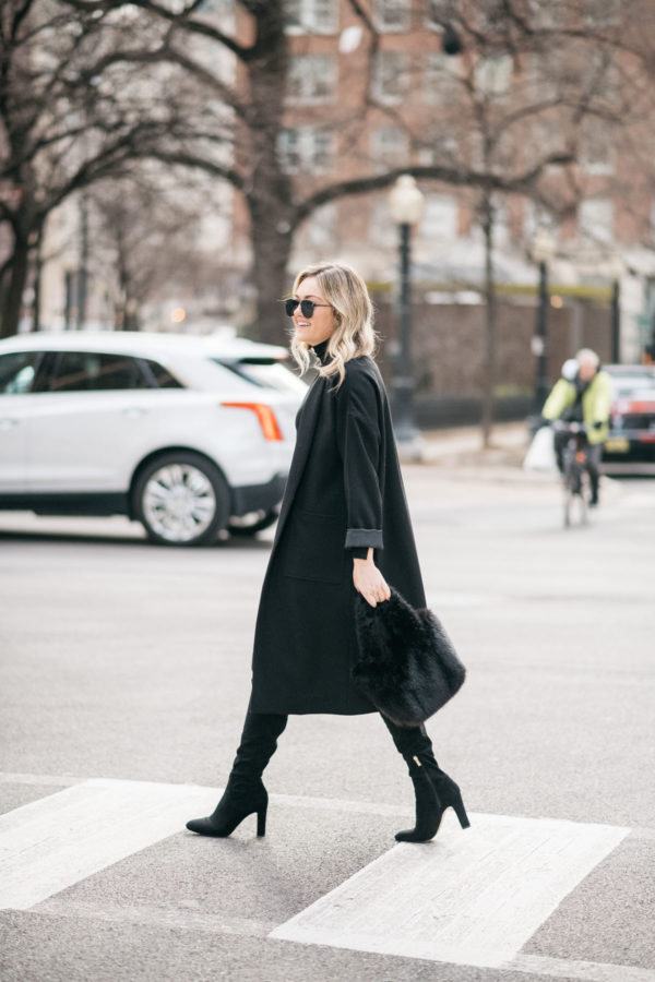 Jessica Sturdy wearing a Les Petites long black crepe coat with a J.Crew shearling handbag, over the knee boots, and Le Specs matte black aviators.