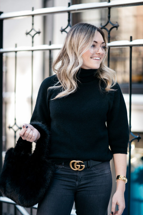 Jessica Sturdy, a Chicago fashion and travel blogger, wearing H&M clear glasses, a Max Mara black turtleneck, and a Gucci GG gold logo belt with a J.Crew shearling bag.