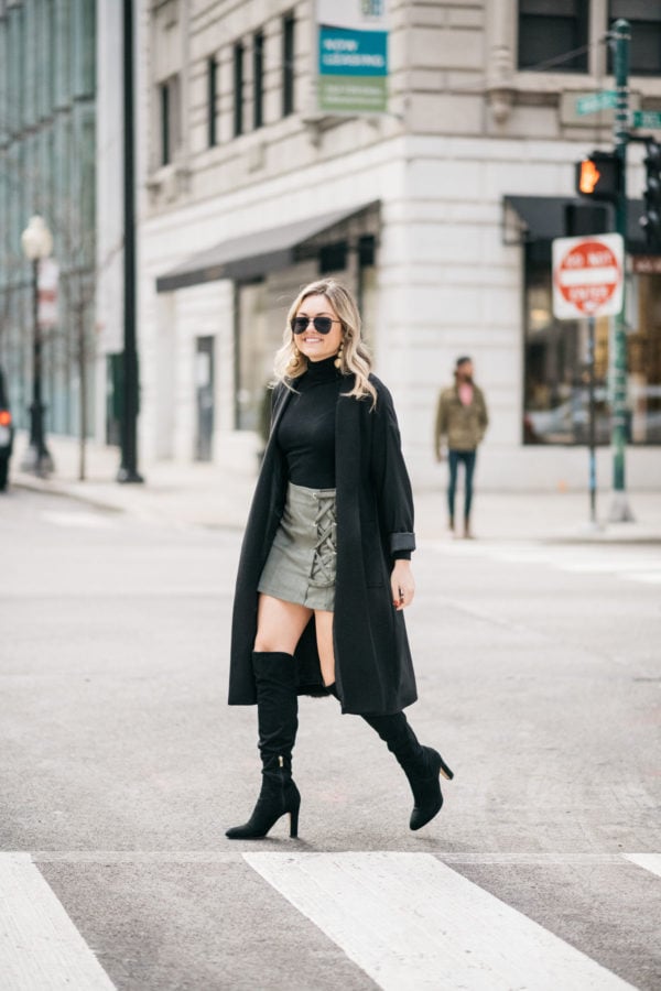 Jessica Sturdy wearing Le Specs matte black aviators, Kenneth Jay Lane earrings, a Zara turtleneck, Les Petites long crepe coat, Kensie olive green skirt, and black over the knee boots with a J.Crew shearling handbag.