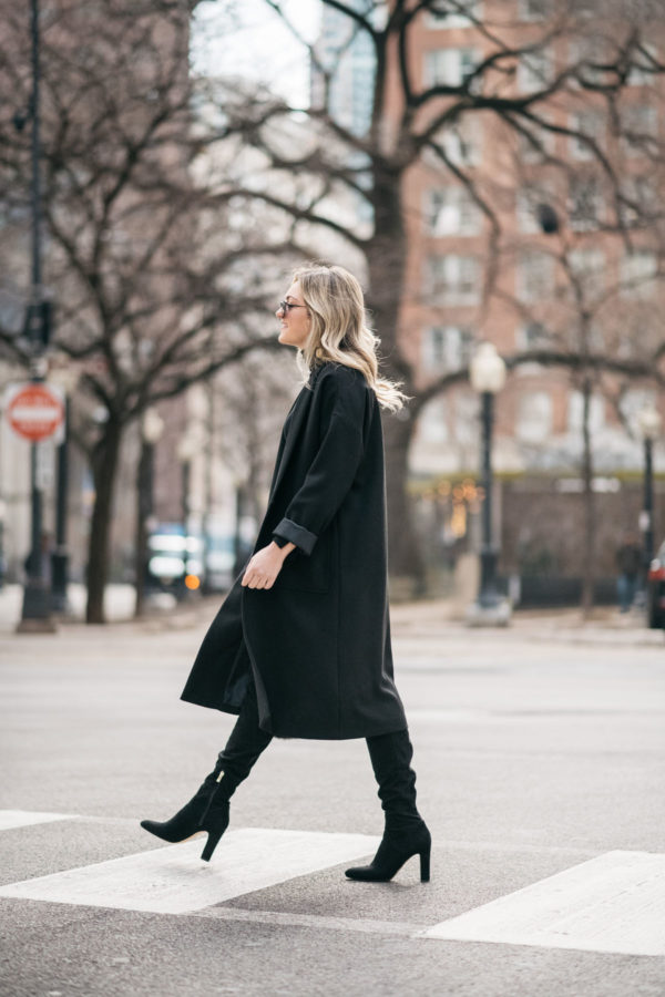 Jessica Sturdy wearing a Les Petites long black crepe coat with a J.Crew shearling handbag, over the knee boots, and Le Specs matte black aviators.
