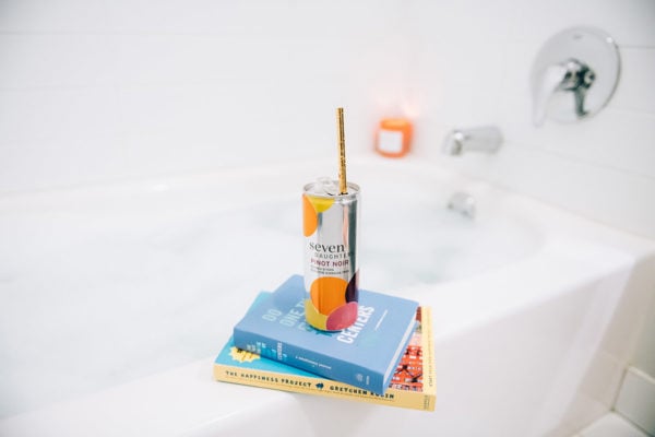 Seven Daughters Pinot Noir can in the bathtub with books and a candle.